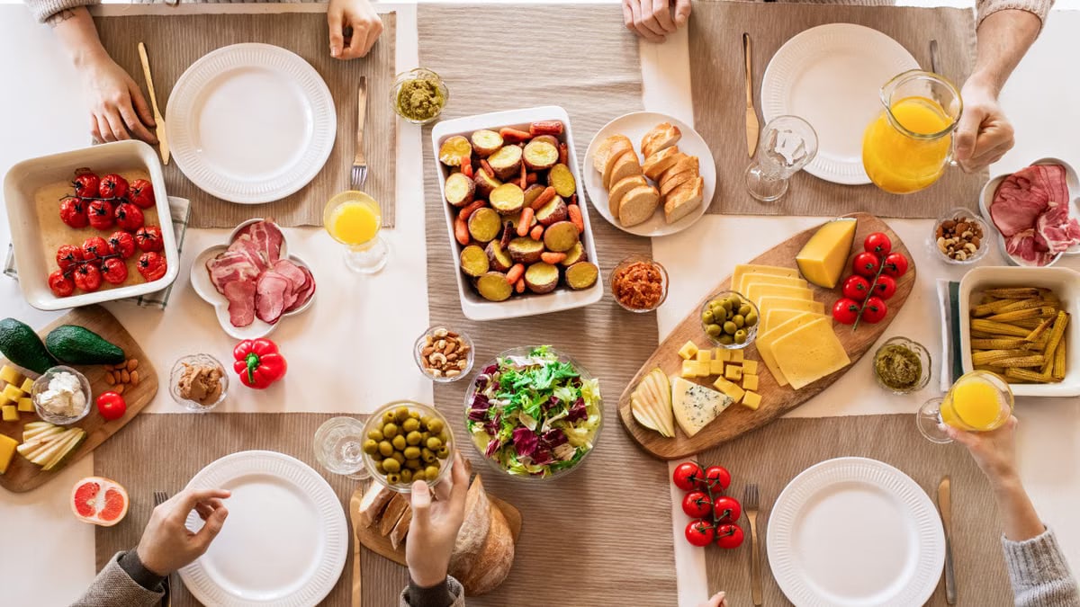 Overhead view of a lively brunch setup with assorted foods, cheeses, and juices on a table.